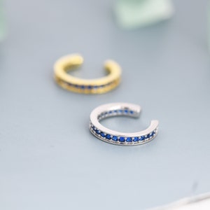 May include: A pair of ear cuffs with a row of blue gemstones. One ear cuff is silver and the other is gold.