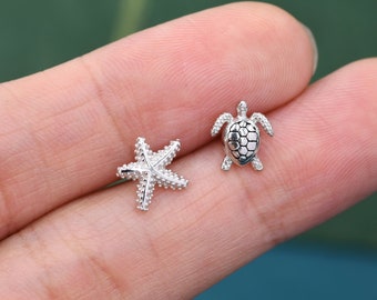 May include: A pair of silver earrings featuring a starfish and a turtle design. The earrings are small and delicate, perfect for everyday wear.