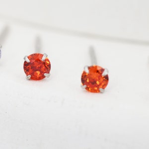 May include: Two small orange gemstone earrings with silver posts.