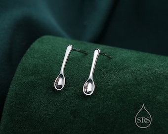 May include: A pair of silver spoon-shaped earrings on a green background.