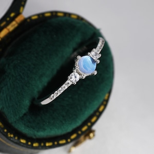 May include: A silver ring with a light blue gemstone and small clear stones set in a delicate band.