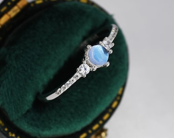 May include: A silver ring with a light blue gemstone and small clear stones set in a delicate band.