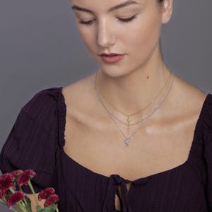 May include: A layered necklace set consisting of three delicate chains. The top chain is gold-toned with a lightning bolt pendant. The middle chain is silver-toned with a small cross pendant. The bottom chain is silver-toned with a dragon pendant.