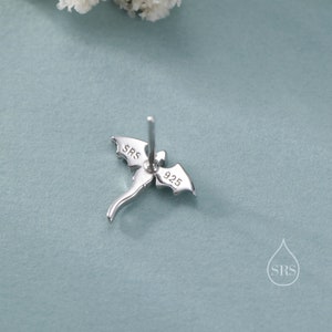 K&ouml;nnte beinhalten: Silberner Ohrstecker in Drachenform mit den Markierungen "SRS" und "925". Der Ohrring hat einen Stecker zum Einsetzen und ist vor einem hellblauen Hintergrund platziert. Das Design umfasst Fl&uuml;gel und einen Schwanz.