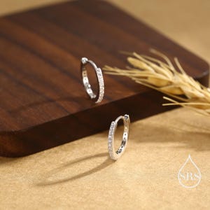 May include: A pair of silver hoop earrings with a row of clear cubic zirconia stones around the edge.