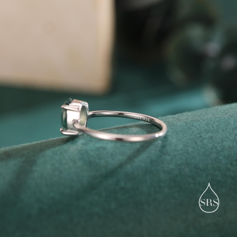 May include: A silver ring with a green gemstone. The ring is on a green surface. The ring is marked "SKS 925".