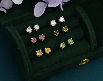 May include: A green velvet box with a variety of gemstone earrings. The earrings are arranged in rows and include clear, pink, green, and yellow gemstones.