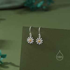 May include: A pair of silver dangle earrings with a daisy design. The center of the daisy is gold.