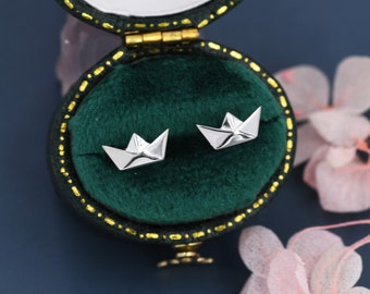 May include: A pair of silver paper boat earrings in a green velvet jewelry box. The earrings are small and delicate, and they are perfect for adding a touch of whimsy to any outfit.