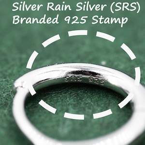 May include: Close-up of a silver ring with the inscription "SRS 925" on the inside. The ring is on a green surface.