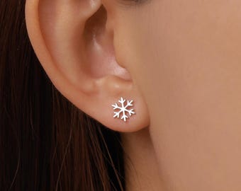May include: A small, silver-toned stud earring shaped like a six-pointed snowflake. The earring features a polished metallic finish with delicate, symmetrical branches extending from the center, securely positioned on the earlobe.