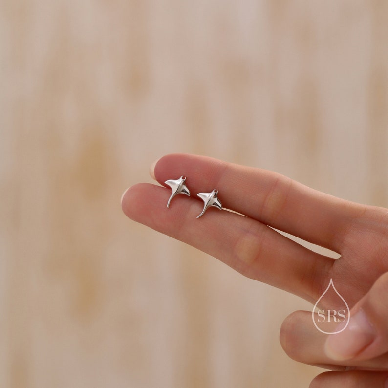 May include: A pair of silver earrings shaped like stingrays. The earrings are small and delicate, and they are perfect for adding a touch of whimsy to any outfit.