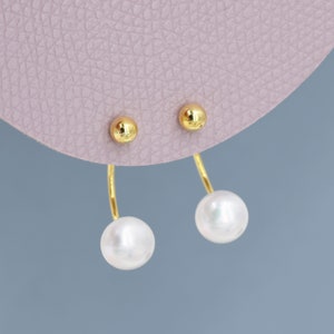Pode incluir: Um par de brincos de ouro com uma pérola pendurada em cada brinco.