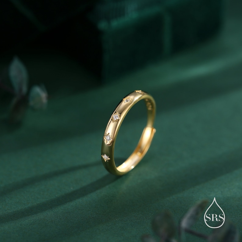 May include: A gold ring with small clear stones set in a star shape around the band.