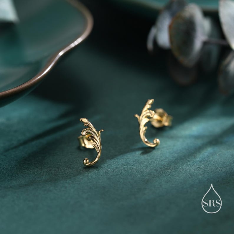 May include: A pair of gold-toned leaf-shaped stud earrings on a green surface.