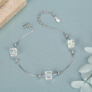 May include: A silver-toned chain bracelet featuring three clear, faceted cube-shaped beads interspersed with small silver-toned spherical beads. The bracelet includes a delicate link chain, a circular spring ring clasp, and an adjustable extender chain.