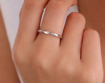 Peut inclure: Une fine bague en métal argenté poli présentant une texture torsadée ou en forme de corde continue sur tout l'anneau. Le métal possède une finition lisse et réfléchissante qui capte la lumière, créant un motif répétitif subtil sur la circonférence.