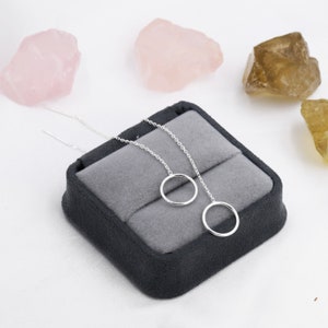 May include: A pair of silver dangle earrings with a simple circle design. The earrings are displayed in a gray velvet box.