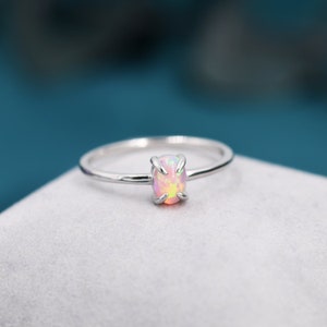 Peut inclure: Une bague en argent ornée d'une pierre d'opale ovale. L'opale présente des nuances de rose, de jaune et de blanc. La fine monture de la bague maintient la pierre avec quatre griffes.