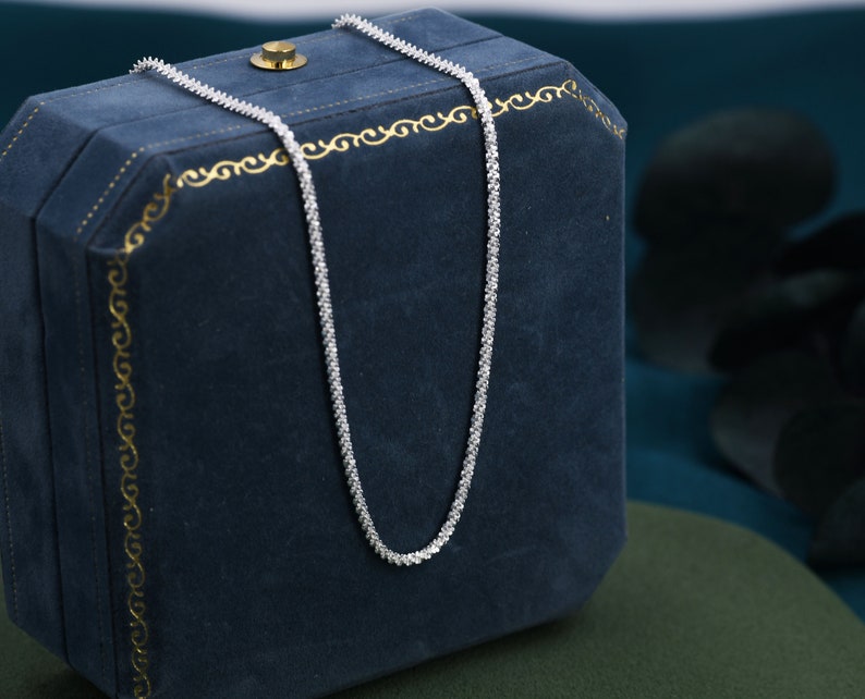 Puede incluir: Un collar de cadena de plata con un dise&ntilde;o delicado y brillante. El collar se muestra en una caja de joyer&iacute;a de terciopelo azul.