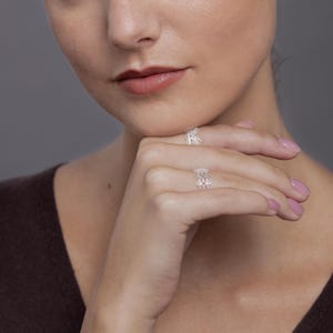 May include: Two silver rings featuring an intricate, openwork filigree pattern. The rings are worn on the index and middle fingers, showcasing a delicate, lace-like metal design that wraps around the finger with a repeating symmetrical motif.