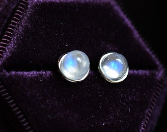 May include: A pair of silver stud earrings with round moonstone gemstones. The earrings are set in a silver bezel setting and have a polished finish.