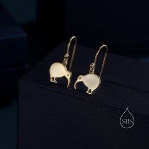 May include: A pair of gold earrings featuring a kiwi bird design. The earrings are made of metal and have a white enamel finish.