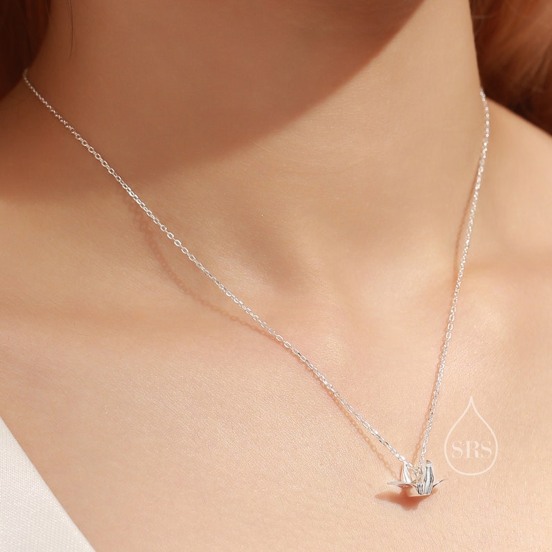 May include: A silver chain necklace with a small origami crane pendant.