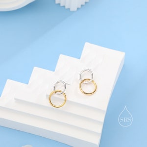 May include: A pair of gold and silver hoop earrings. The earrings are made of two hoops, one larger than the other. The larger hoop is silver and the smaller hoop is gold.
