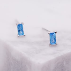 Può includere: Un paio di orecchini a perno d'argento con pietre rettangolari di colore blu chiaro.