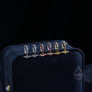 May include: Five pairs of hoop earrings with a bat charm hanging from each hoop. The hoops are silver, rose gold, and gold. The earrings are displayed on a black velvet box.