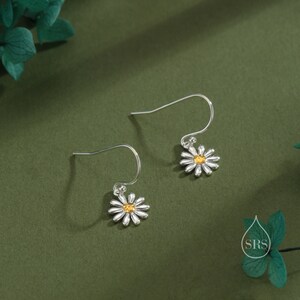 May include: A pair of silver dangle earrings with a small white daisy charm with a yellow center.