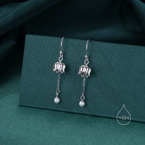 May include: A pair of silver earrings with a delicate flower design and a single pearl dangling from each earring.