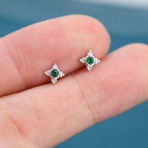 May include: A pair of silver stud earrings with a small green gemstone in the center of each earring. The earrings are surrounded by a small circle of silver beads.