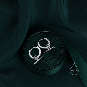 May include: A pair of silver hoop earrings with a small bar attached to each hoop. The earrings are on a green ribbon.