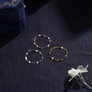 May include: Three silver, gold, and rose gold chain bracelets with a linked oval design. The bracelets are on a dark blue fabric background.