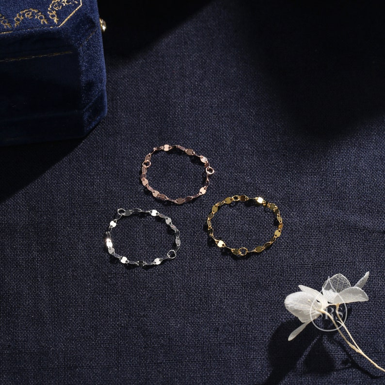May include: Three silver, gold, and rose gold chain bracelets with a linked oval design. The bracelets are on a dark blue fabric background.