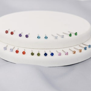 Puede incluir: Un expositor de 18 pares de pendientes de bot&oacute;n con piedras preciosas de varios colores, incluyendo rojo, azul, verde, morado y transparente.