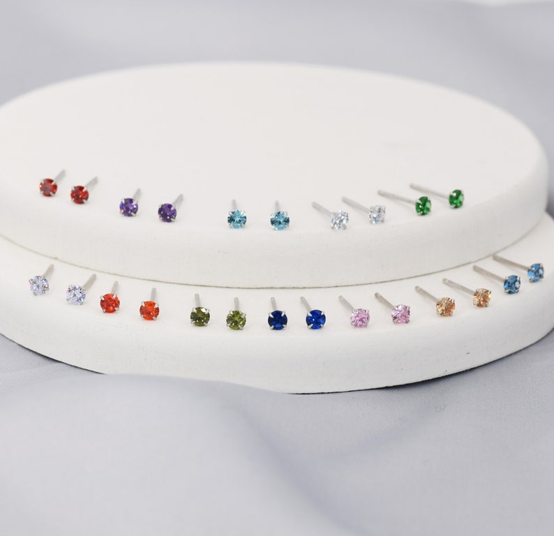 Puede incluir: Un expositor de 18 pares de pendientes de bot&oacute;n con piedras preciosas de varios colores, incluyendo rojo, azul, verde, morado y transparente.