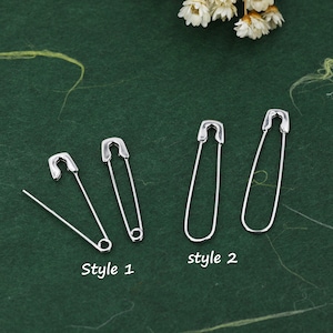 May include: Two styles of safety pins. The first style is a smaller safety pin with a pointed end. The second style is a larger safety pin with a rounded end. The text "Style 1" and "Style 2" is printed below each style of safety pin.