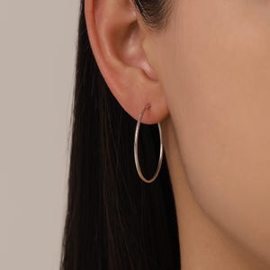 Peut inclure: Gros plan d'une boucle d'oreille créole argentée portée à l'oreille. La boucle d'oreille est un design simple en métal poli. La boucle d'oreille est un bijou classique.