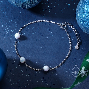 May include: A silver chain bracelet with three white opal beads. The bracelet has a lobster clasp and an extension chain.