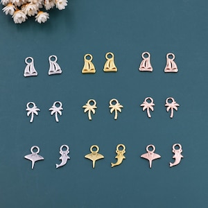 May include: A selection of miniature charms in silver, gold, and rose gold. The charms feature designs of sailboats, palm trees, stingrays, and dolphins. They are displayed on a teal background, suitable for crafting jewellery.