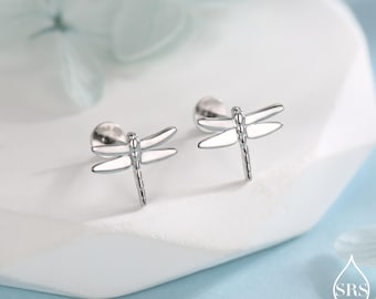 May include: A pair of silver dragonfly stud earrings. Each earring features a detailed dragonfly design with delicate wings and a slender body. The earrings are displayed on a white surface, with a soft, blurred background.