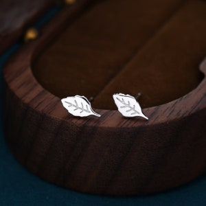 Può includere: Un paio di orecchini a lobo in argento a forma di foglia. Gli orecchini sono piccoli e delicati, con un design semplice.