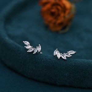 Può includere: Un paio di orecchini d'argento con un delicato design a foglia. Ogni orecchino presenta una fila di piccole pietre di forma marquise chiare incastonate in una forma curva.