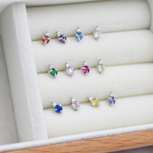 May include: A set of 10 small stud earrings with a single gemstone and two smaller clear stones. The gemstones are in a variety of colors, including red, purple, blue, green, pink, and yellow.