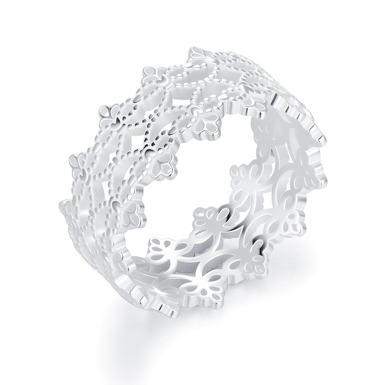 May include: A silver-toned ring featuring an intricate, openwork filigree pattern that resembles lace. The band has a scalloped, crown-like edge with repeating floral-inspired motifs throughout the entire circumference of the metal ring.