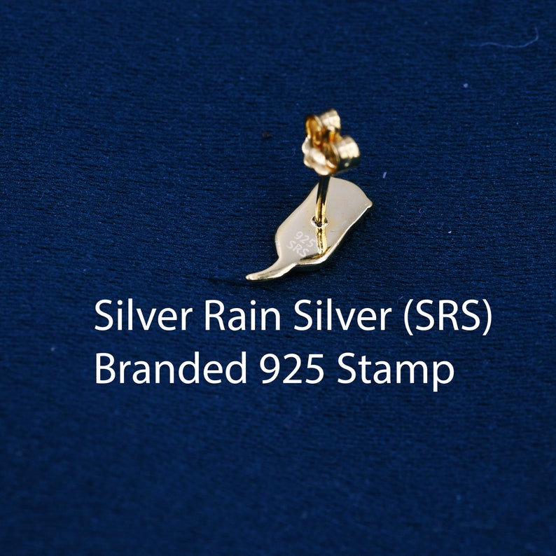 May include: A gold-colored earring with a post and a back. The earring has a 925 stamp on the back, indicating it is made of sterling silver. The earring is on a blue background.
