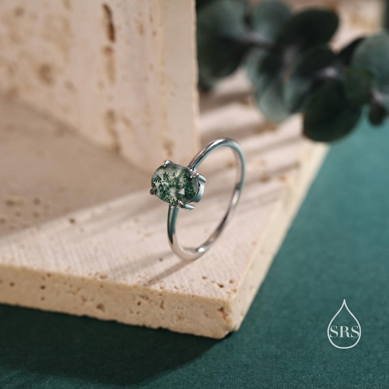 May include: A silver ring with a green moss agate oval stone.